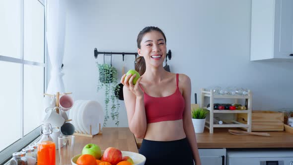Asian attractive active woman pick up a green apple in kitchen at home enjoy eat healthy foods.