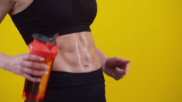 Woman Holds a Sports Shaker with Water in Hand and Shows the Muscles of the Abdomen Closeup