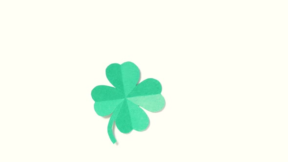 A leaf of clover cut out of paper is spinning on a shiny green background.