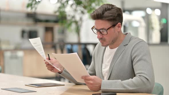 Focused Middle Aged Man Reading Documents in Office 