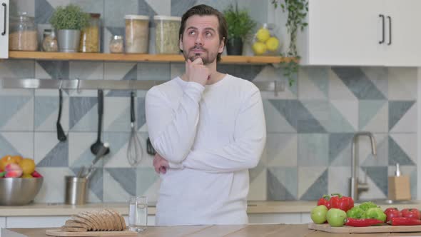 Serious Young Man Thinking While Standing in Kitchen