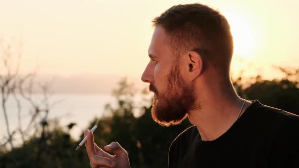 Bearded Redhead Man Smokes a Cigarette at Sunset and Looks at the Camera. Handsome Business Man on