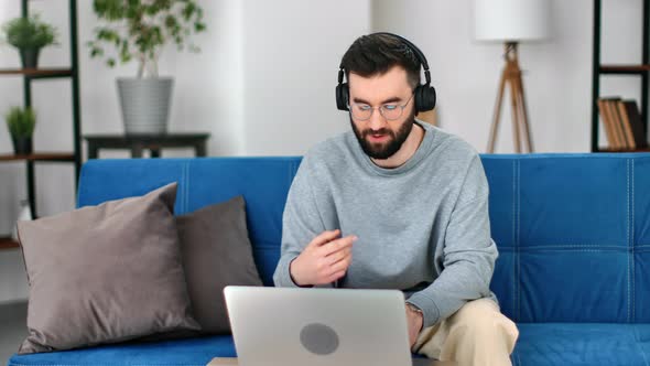 Modern Freelancer Business Man in Headphones Talking Online Video Call Use Laptop on Blue Couch