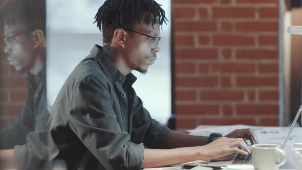 Happy Black Man Using Laptop and Smiling at Camera while Working in Loft Office