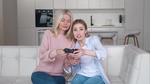 Happy Grown Daughter Teach To Play Video Games on Console While Sitting on Couch in Front of Tv