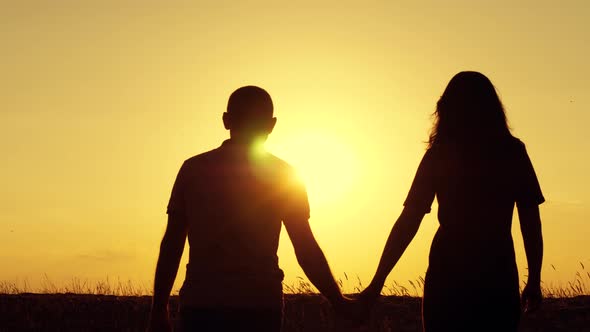 A Man and a Woman Hold Hands and Walk To Meet the Setting Sun. Happy Family, Relationships