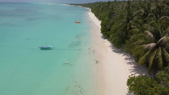 Aerial view of the Maldivian coast and island with a parked yacht on turquoise water