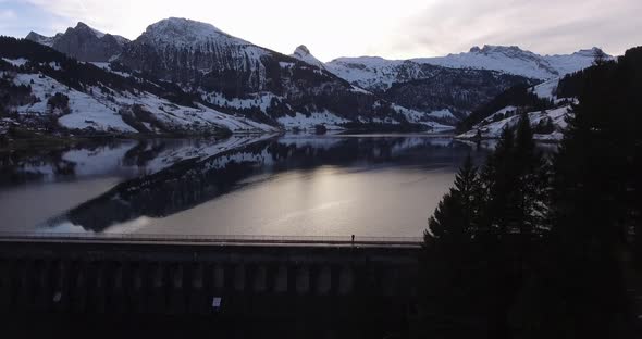 Big winter mountain panorama on an artificial lake with one guy on the dam in Switzerland.