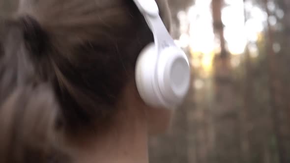 A Girl Jogs in the Park and Listens to Music on Headphones