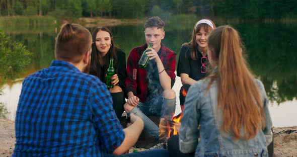 Friends Sit Around Bonfire Talking and Drinking Beer on Sandy Beach Young Mixed Race Group of Men