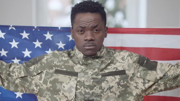 Portrait of Proud Young Confident Military Man Wrapped in American Flag Looking at Camera and