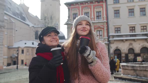 Two Smiling Women Tourists Traveling Together Drinking Hot Tea Coffee From Cups on City Street