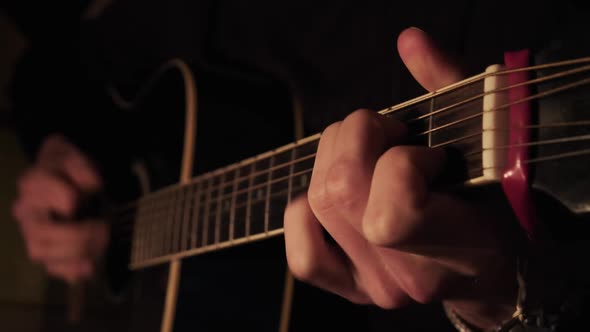 Man Playing Acoustic Guitar at Home in Atmospheric Dark Warm Lighting