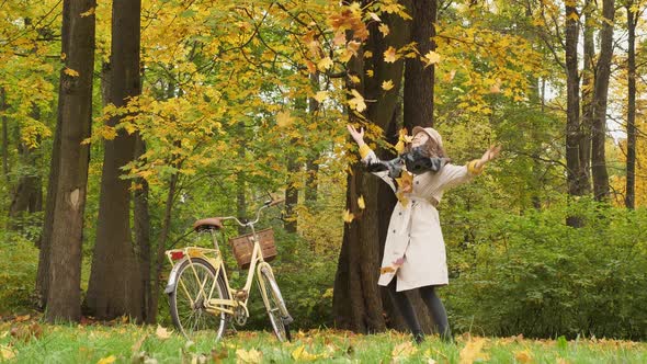 Young Woman Has Fun Throwing Up Fallen Leaves in Autumn Park