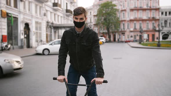 Portrait of Young Guy in Protective Face Mask Riding Bike in the Street of Empty City Center Slow