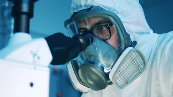 Laboratory Specialist in a Hazmat Suit is Looking Into a Microscope