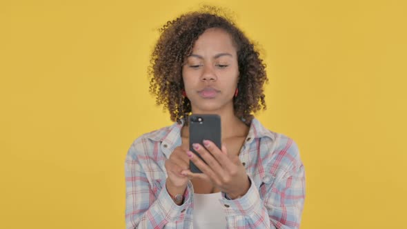 Young African Woman Browsing Smartphone on Yellow Background