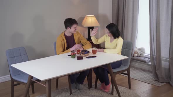 Top View of Cheerful Caucasian Mother and Son Giving High Five and Talking. Happy Woman Drinking Tea