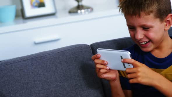 Boy using mobile phone while upset sister sitting besides him in living room