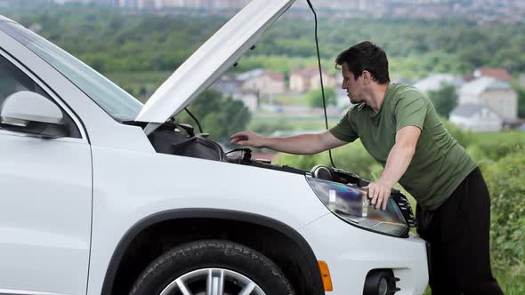 Young man standing near broken down car with popped up hood having trouble with her vehicle.