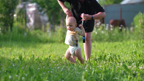 Mom and Baby Walk Hand in Hand on the Green Grass