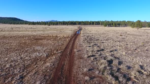 Aerial Over Red Dirt Road in Desert Fields By Mountains