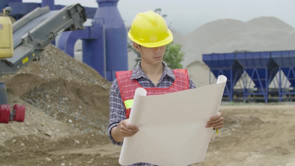 Architect In Construction Site Looking At Blueprint alt