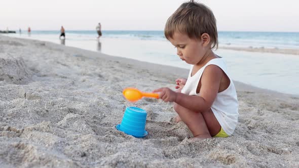 Boy Playing with Toys on the Beach Building Beads and Turrets Smiling at Someone Behind the Scenes