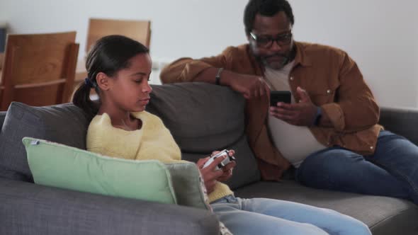 Bored African girl playing the console while his father calling someone