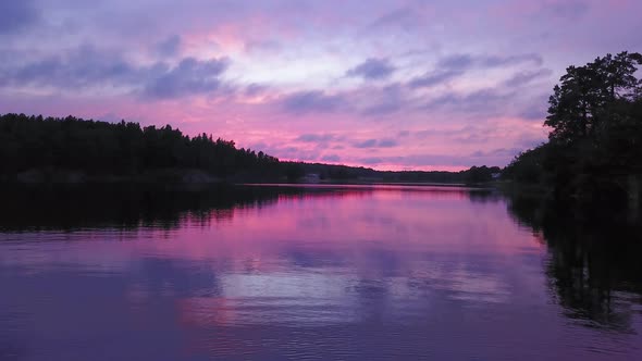 Aerial drone shot close to the water, above a lake and towards the forest, a purple sky, at a colorf