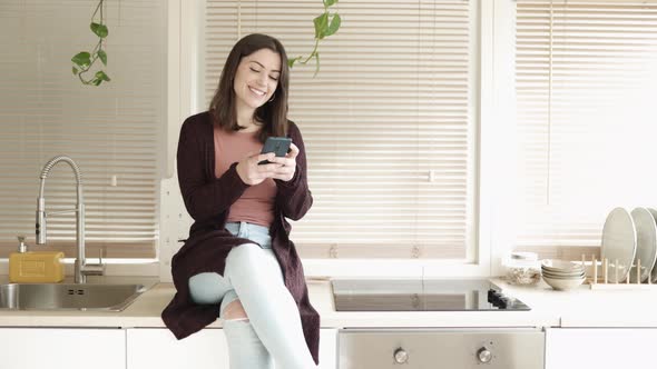 Happy Hispanic Woman Using a Cell Phone in the Kitchen