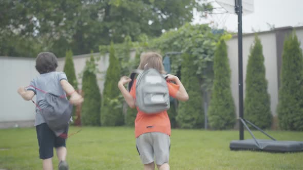 Back View Wide Shot of Cheerful Schoolboys Running Home and Throwing Up Backpacks. Joyful Caucasian