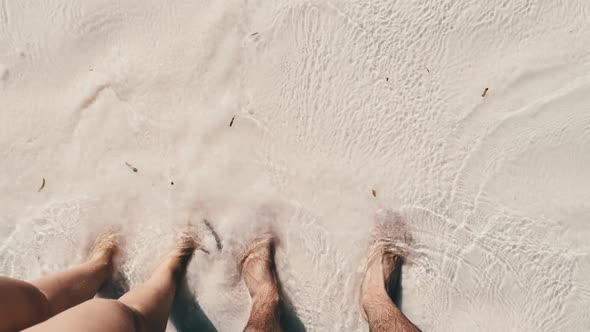 POV Legs of a Young Couple Standing on White Sand and Surf Waves of Ocean Shore