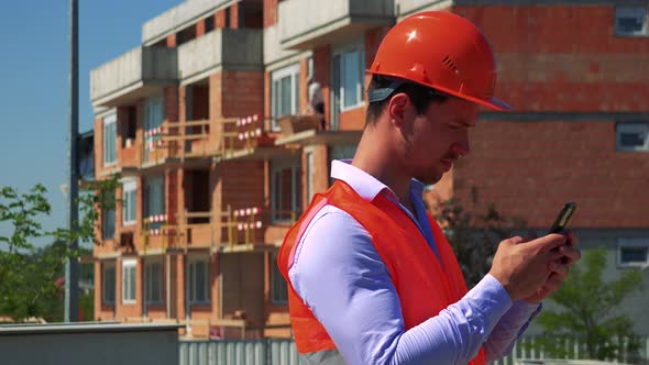 Construction Worker Works on the Smartphone in Front of Building Site
