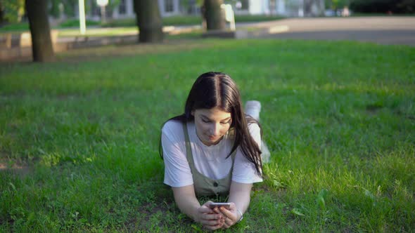 Attractive Woman Lies on Grass in Park Use Smartphone Relaxing Summer Vacation