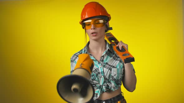 Female Engineer in an Orange Safety Helmet is Shouting Through a Megaphone