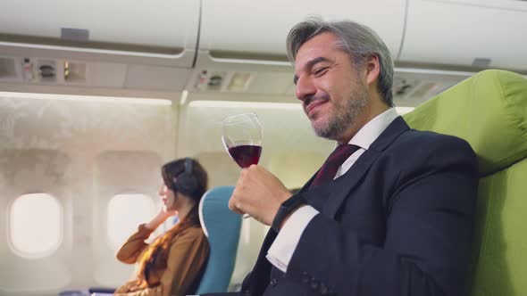 Caucasian smart businessman sitting in business class smelling and drinking red wine on airplane.