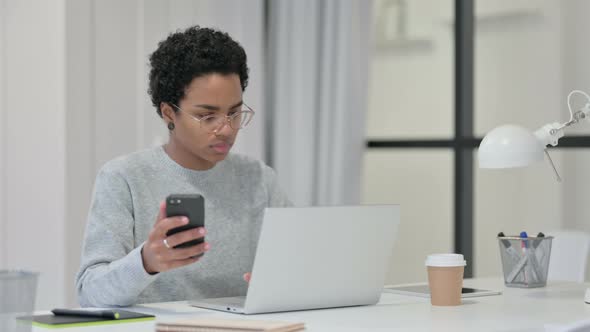 African Woman with Laptop Using Smartphone at Work