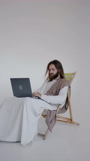 Jesus Sits in a Schizlong and Works at a Computer on a White Background