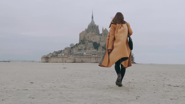 Rear View Zoom in on Fashionable Tourist Woman Slowly Walking on Sea Sand at Epic Mont Saint Michel
