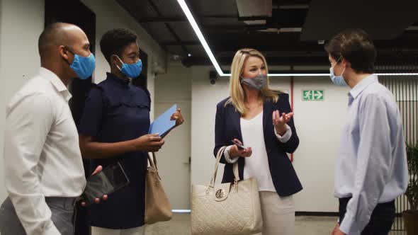 Diverse business people wearing face masks talking in office