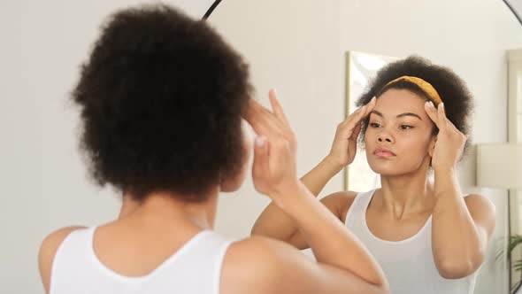 African american woman makes herself a face lifting massage in front of a mirror