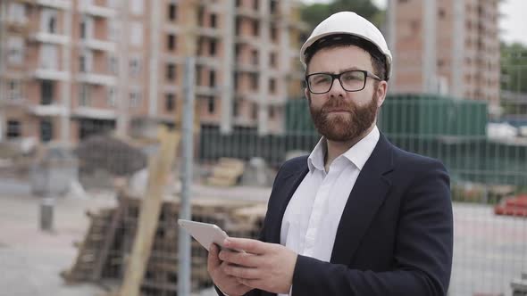 Portrait of Young Businessman with Tablet on Construction Site Looking To Camera Wearing a Safety