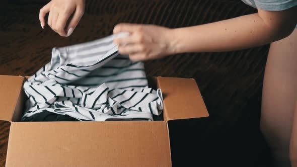 Young Girl Disassembles a Parcel With Things and Examines Clothes