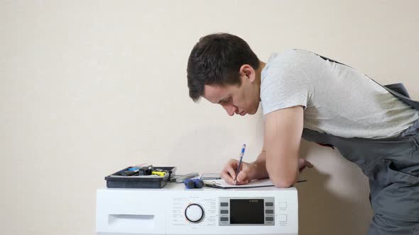 Man Writes on Clipboard Examining Modern Washing Machine