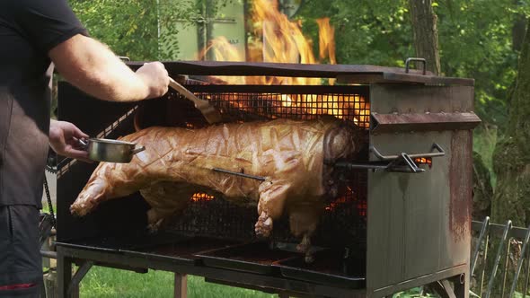 Man Brushes Roasting Piglet with Sauce Standing in Garden