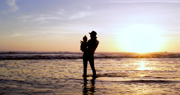 A woman enjoys sunset at the beach in 4k with her child and the beautiful sunset as her backdrop.