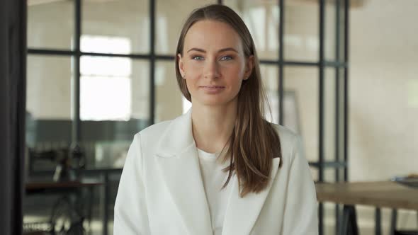 Pretty Happily Smiling Woman Looking Into the Camera is Sitting at a Desk in the Office