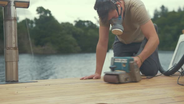 Carpenter sanding roof of wooden boat using belt sander. MEDIUM CLOSE UP