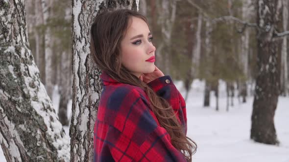 Young Woman with Wavy Hair Standing and Touching Face in Winter Forest